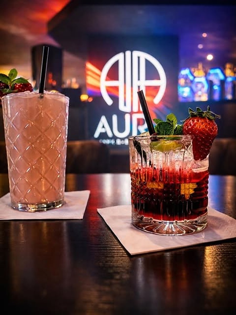 Zwei Cocktails mit Erdbeere und Limette vor dem leuchtenden AURA-Logo an der Bar